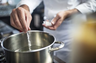 Chef putting types of salt in pan of water on stove, close-up