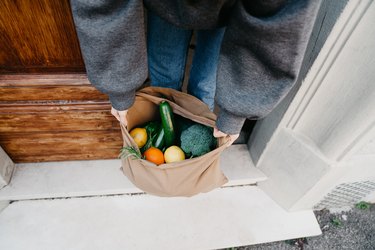 Young woman is picking up a bag of vegetables and fruit just delivered to her home