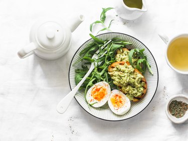Healthy breakfast or snack - boiled egg, arugula salad and avocado toast on a light background, top view