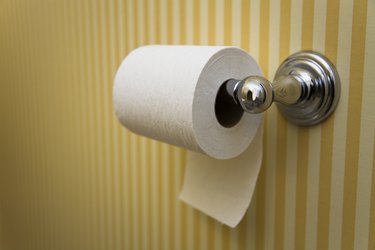 Toilet paper roll hanging in a bathroom with striped yellow wallpaper
