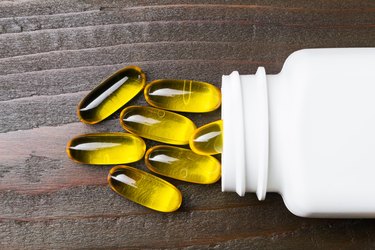 Yellow capsules omega 3, fatty acid, fish oil with white bottle on dark wooden table, macro image, top view