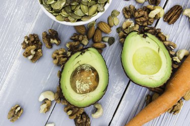 Healthy food and dieting concept. Focus on avocado. Carrots, nuts: cashews, almonds, pecans, walnuts, pumpkin seeds on a wooden table. Light summer flat lay food