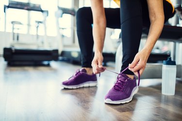 lower section of woman tying purple sneaker in a gym