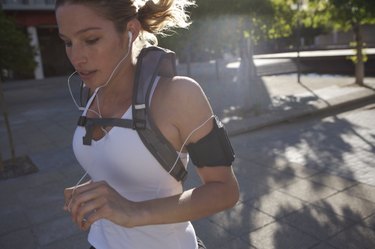 Woman jogging outdoors with backpack and earphones, close-up