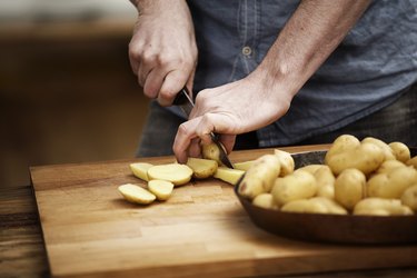 close up of man cutting potatoes on wooden cutting board