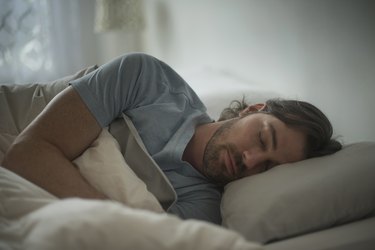 a person sleeping on their side in bed wearing a blue t-shirt