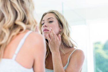 Focused beautiful young woman looking at herself in the bathroom mirror