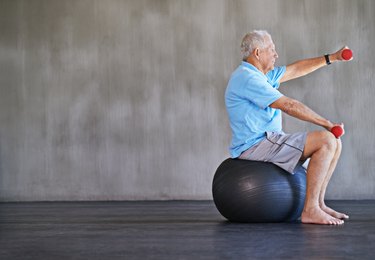 older man on stability ball doing reps and sets of single-arm dumbbell front raises