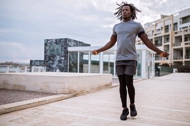 Athletic man performing double unders with a jump rope outdoors.