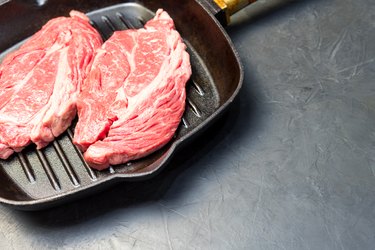 A raw marbled beef steak sits in a frying pan.