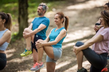 Group of happy athletes stretching their legs on a sports training at the park.