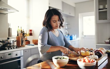 a young adult meal prepping lunch by cutting vegetables in the kitchen