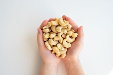 Healthy eating, dieting, vegetarian food concept. Close up of kid hands holding peeled cashew on white background