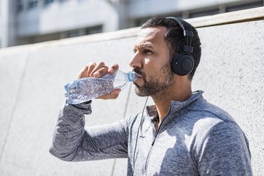 Man having a break from exercising wearing noise-cancelling headphones and drinking from bottle