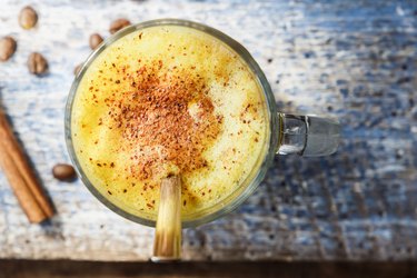 Golden milk latte with turmeric in a glass strewed with cinnamon, on a blue wooden background