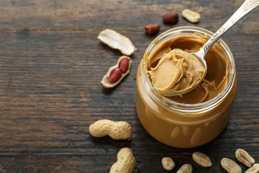 peanut paste in an open jar and peanuts