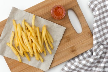 French fried potatoes on cutting board with sauce top view.