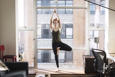 Portrait of confident woman practicing tree pose by window at home
