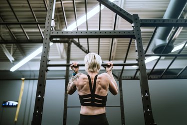 shot of a woman's back muscles while doing a chin up exercise to burn calories in a workout