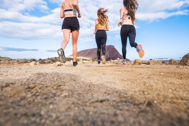 group of beautiful back view of females runners doing sport activity jogging in outdoor. mountain in background and enjoy the healthy leisure activity together. ground view and blue sky