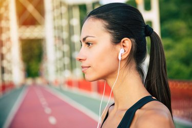 Woman in sportswear and headphones on track listening to cardio workout playlist