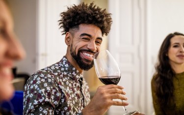 Smiling man drinking red wine during dinner party at home