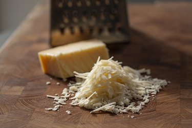 Grated italian parmesan cheese on wooden chopping board with a block of Parmesan and a grater in the background to bread proteins on a low-carb diet