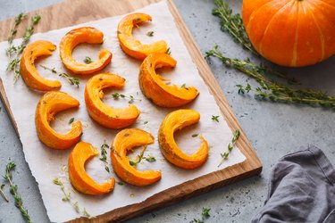 Baked pumpkin slices with thyme on a wooden board over grey table. Seasonal food vegetarian recipe.