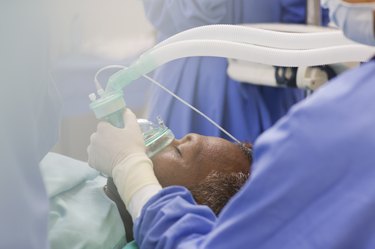 Close up of doctor wearing surgical gloves, holding oxygen mask over patient in operating theater administering sedation for colonoscopy