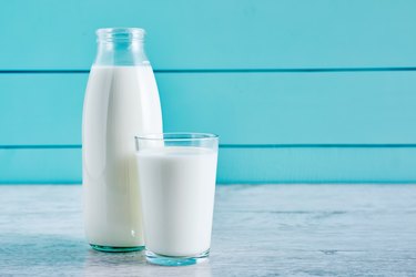 Bottle of milk and a glass full of milk on a wooden table against turquoise wooden background. Close up view.