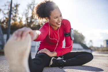 Woman stretching outside wearing arm band and headphones