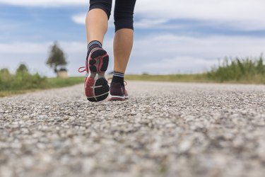 Feet of woman running on remote country lane in summer