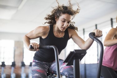 Determined young woman riding elliptical bike in gym