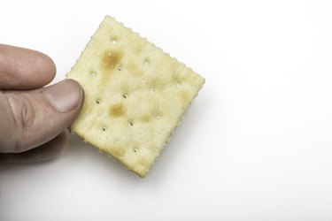 a close up of a person's hand holding a saltine cracker