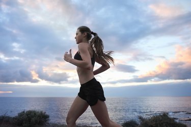 Young woman running near ocean with cloudy sky