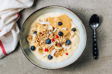 Morning healthy breakfast bowl with yogurt, muesli, blueberry, banana, coconut on the concrete background.