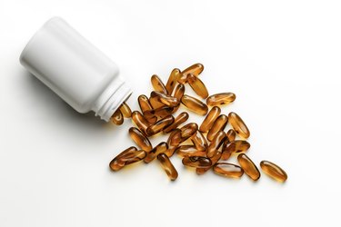 Close up of fish oil vitamin gelatin capsules with Omega-3 and plastic bottle laying on white background