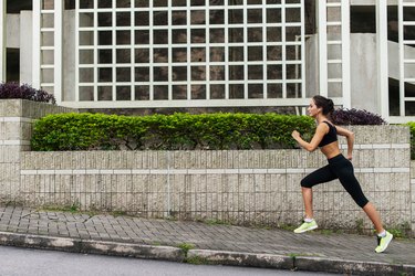 Side view of young female runner listening to music and jogging on sidewalk in town