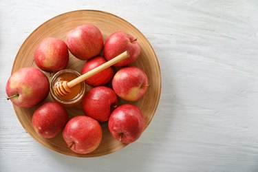 Ripe juicy apples with honey on wooden plate