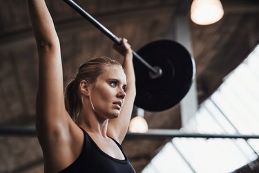 Young woman lifting weights over her head in a gym
