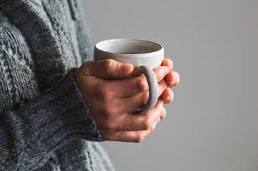 Person in woolly gray sweater holding warm cup of tea
