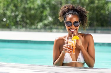 Fashion beauty woman in pool drinking cocktail