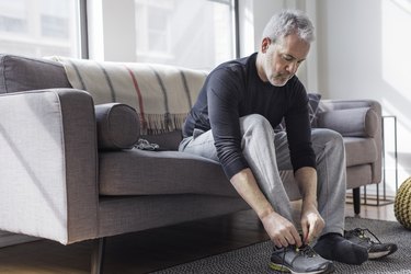 man tying shoe sitting on couch before full-body workout for beginners