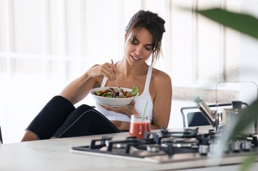 Person eating salad and drinking fruit juice in the kitchen at home.