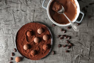 Plate with sweet truffles, ganache and cacao powder on grey table