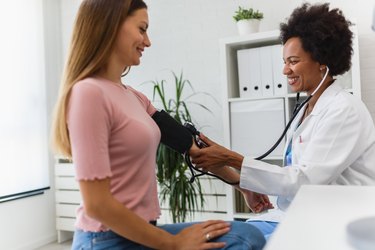 Female African American doctor measuring blood pressure of a young woman