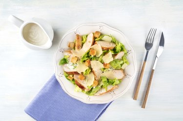Chicken Caesar salad plate. Chicken breast, green lettuce, Parmesan cheese, and croutons, with the typical dressing, shot from the top with a place for text