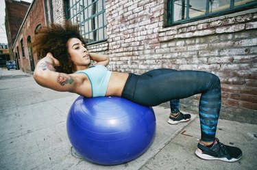 Hispanic woman balancing on fitness ball near brick wall