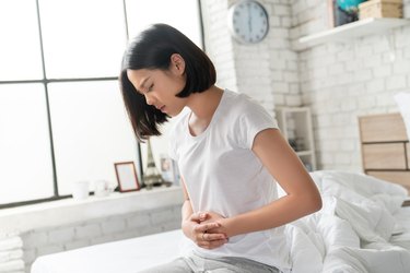 Asian women sitting in bed holding stomach with digestive problem