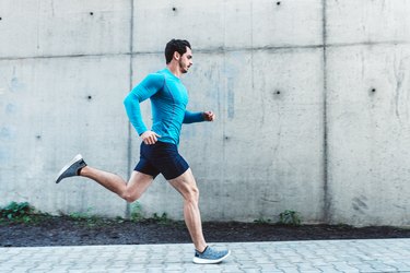 fit young man wearing a blue long-sleeve shirt and running outdoors